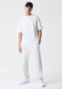 Camiseta blanca de algodón con mangas cortas y pequeño logo en el pecho, combinada con pantalones jogger de algodón blancos y zapatillas blancas.