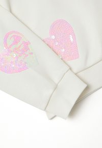 Witte sweatshirt met roze iriserende pailletten harten op beide mouwen. Voorzien van geribbelde manchetten en een zachte textuur.
