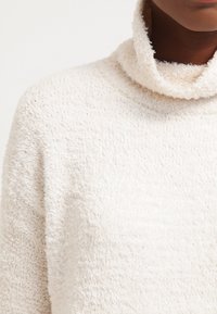 Pull à col roulé blanc duveteux avec une finition douce et texturée, doté d'un col haut et d'une coupe décontractée pour le confort.