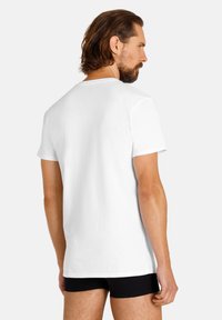 Maglietta bianca in cotone con maniche corte, colletto tondo e design semplice, indossata con pantaloni corti neri, mostrata nella vista dal dietro.