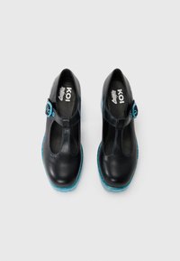 Chaussures en cuir noir avec un design à sangle T, présentant une boucle d'accent bleu et une semelle bleue translucide. Texture lisse avec une couture subtile.