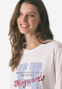 T-shirt bianca in cotone con testo blu e rosso, "Scuola di Magia e Stregoneria di Hogwarts," con scollatura rotonda e maniche corte.