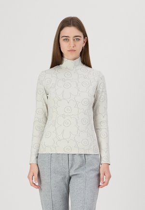 Langermet, høyhalset topp i lys kremfarge med grå blomsterdesign, laget av myk stoff. Kombinert med grå bukser.