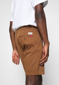 Shorts en coton marron à coupe droite, avec une poche arrière, des détails de couture subtils, et une étiquette de logo Levi's sur la taille.