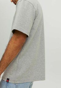 Sivá bavlnená tričko s krátkym rukávom a voľným strihom. Obsahuje malú farebnú značku na spodnom leme a viditeľné švy.