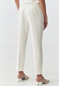 White tailored trousers with a straight fit, two back pockets, and a smooth fabric texture. Paired with light-colored heeled shoes.