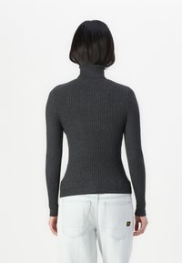 Tett, mørkegrå ribbestrikket høyhalset genser med lange ermer. Myk tekstur og en slank silhuett. Brukt med lyseblå jeans.