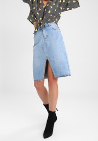Light blue denim skirt with a front slit, frayed hem, paired with a black patterned blouse and black ankle boots.