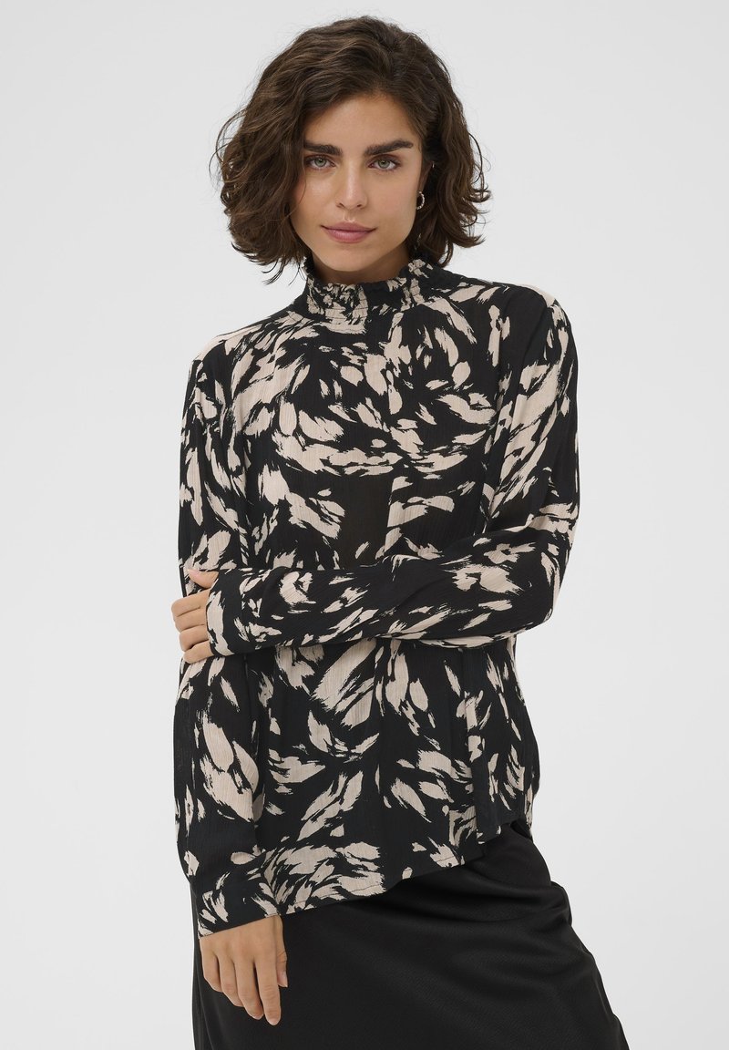 Juoda marškinėliai su abstrakčiais smėlio spalvos raštais, aukštu raukiniu apykakle, ilgomis rankovėmis ir laisvo silueto. Pagaminti iš lengvos tekstūruotos medžiagos.