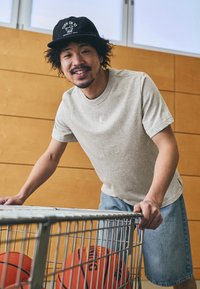 Gray cotton t-shirt with short sleeves and a small logo, paired with denim shorts, positioned by a wire basket holding basketballs.