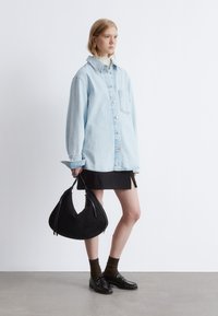 Light blue denim oversized shirt with a pocket, black mini skirt, black suede handbag, brown socks, and black loafers. Simple and modern styling.