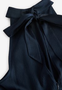 Primo piano di un indumento senza maniche blu navy con un grande fiocco di stoffa annodato sullo scollo.