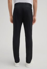 Marineblauwe broek met een getailleerde pasvorm, voorzien van twee achterzakken met knopen, een geplooide voorkant en zijzakken. Gepaard met witte schoenen.