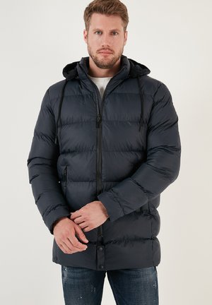Giacca imbottita blu navy con cappuccio, dotata di zip frontale, cordini e tasche laterali. Texture liscia, rifinita con chiusura a bottone.