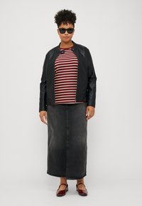 Svart skinnjakke med jevn tekstur, burgunder og hvite stripete skjorte, lang svart denimskjørt, og røde slip-on sko. Solbriller inkludert.