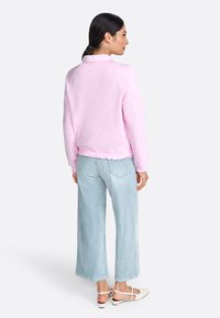 Felpa rosa chiaro con orlo a scallop, abbinata a jeans a gamba larga azzurri e scarpe beige. Tessuto morbido, vestibilità rilassata.