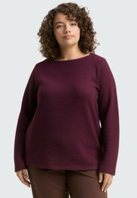 Pull en bordeaux à manches longues, col rond, en tissu texturé, coupe décontractée, associé à un pantalon marron. Design simple, sans motifs visibles.
