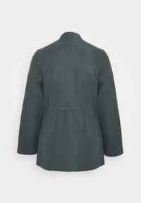 Chaqueta de color verde oscuro con un diseño sencillo, mangas largas, escote redondo y una costura en la cintura para dar forma. El material parece suave y ligero.