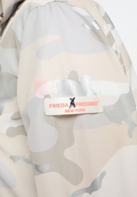 Lekka, beżowa kurtka z kamuflażem z połyskującymi akcentami. Posiada metkę z napisem "FRIEDA FREDDIES® NEW YORK" oraz logo zwierzęce na ramieniu.