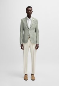 Blazer texturé vert clair avec chemise blanche, pantalon crème et mocassins beige. Accent notable d'un bouton en argent sur le blazer.