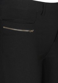 Schwarze Hose mit einem Reißverschluss vorne, glattem Stoff und einer figurbetonten Passform. Sichtbare Nähte entlang der Seitennähte.