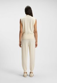 Sleeveless, cream-colored knit top with a high neckline, paired with matching tapered pants. Soft texture; minimalist design without patterns.