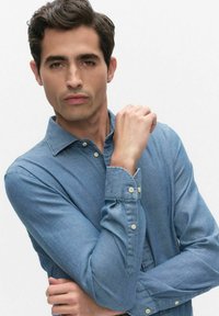 Lichtblauw denim overhemd met een button-down kraag en lange mouwen. Heeft een subtiele textuur en knopen bij de manchetten voor aanpassing.