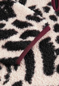 Gros plan d'un tissu polaire texturé avec motif léopard noir et blanc et détail de la bordure en tissu bordeaux.