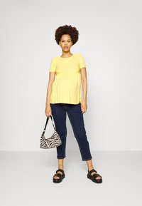 Top amarelo de mangas curtas com detalhes franzidos, jeans azul-escuro, sandálias de plataforma pretas e uma bolsa com padrão de zebra.