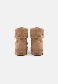 Botines beige con parte superior de lona, borde redondeado y tira en la parte trasera. Cuentan con suela de goma y logotipo grabado en el talón.