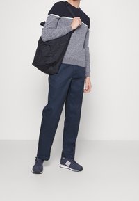 Tenue décontractée avec un pull en maille rayé bleu marine, un pantalon bleu foncé et des baskets bleu marine. Un sac à bandoulière noir matelassé est porté sur une épaule.
