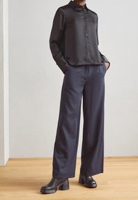 Chemise noire en satin à boutons associée à un pantalon large bleu marine et des bottes noires à talons épais ; texture lisse et coupe décontractée.
