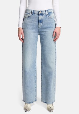 Jean large bleu clair en denim, avec une taille haute, deux poches avant et un ourlet brut. Porté avec des chaussures à talons à motifs.