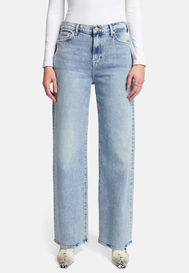 Jeans a gamba larga di colore blu chiaro, realizzati in denim, con vita alta, due tasche frontali e dettagli a orlo grezzo. Abbinati a scarpe con tacco a fantasia.