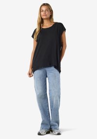 Bluză neagră cu mâneci scurte și croială largă, combinată cu blugi albastru deschis, cu croială dreaptă, și adidași gri. Design simplu, textură moale.