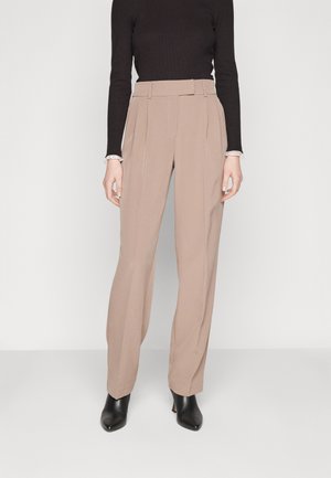 Pantalons tailleurs beiges à taille haute avec plis, fabriqués dans un tissu lisse, associés à un haut noir ajusté à manches longues et des bottes noires à talons.