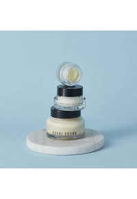 Trois bocaux empilés de crèmes hydratantes Bobbi Brown sur une base circulaire en marbre. Matériaux en verre et en plastique, produit de couleur blanc crémeux, couvercles noirs.