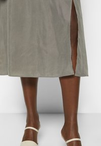 Khadki midi spódnica z bocznymi rozcięciami, gładką fakturą i delikatnym połyskiem. Połączona z minimalistycznymi sandałami w kolorze nude.