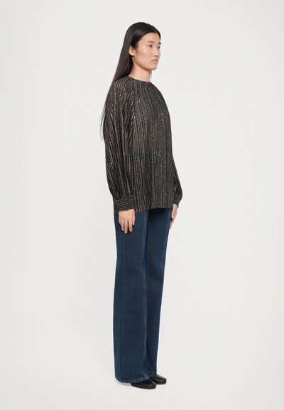 Maglione nero a costine con fili metallici, dotato di scollatura rotonda e maniche lunghe, abbinato a jeans in denim blu a vita alta e gamba larga.