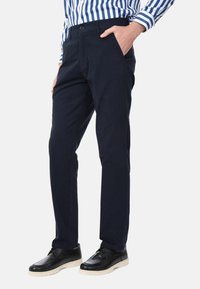 Chino blu navy con una texture liscia, dotati di tasche laterali, passanti per cintura e un design a gamba dritta. Abbinati a scarpe nere e una camicia a righe.