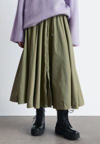 Olive green long skirt with a drawstring waist and zipper front, paired with black lace-up platform boots and a soft lavender sweater.