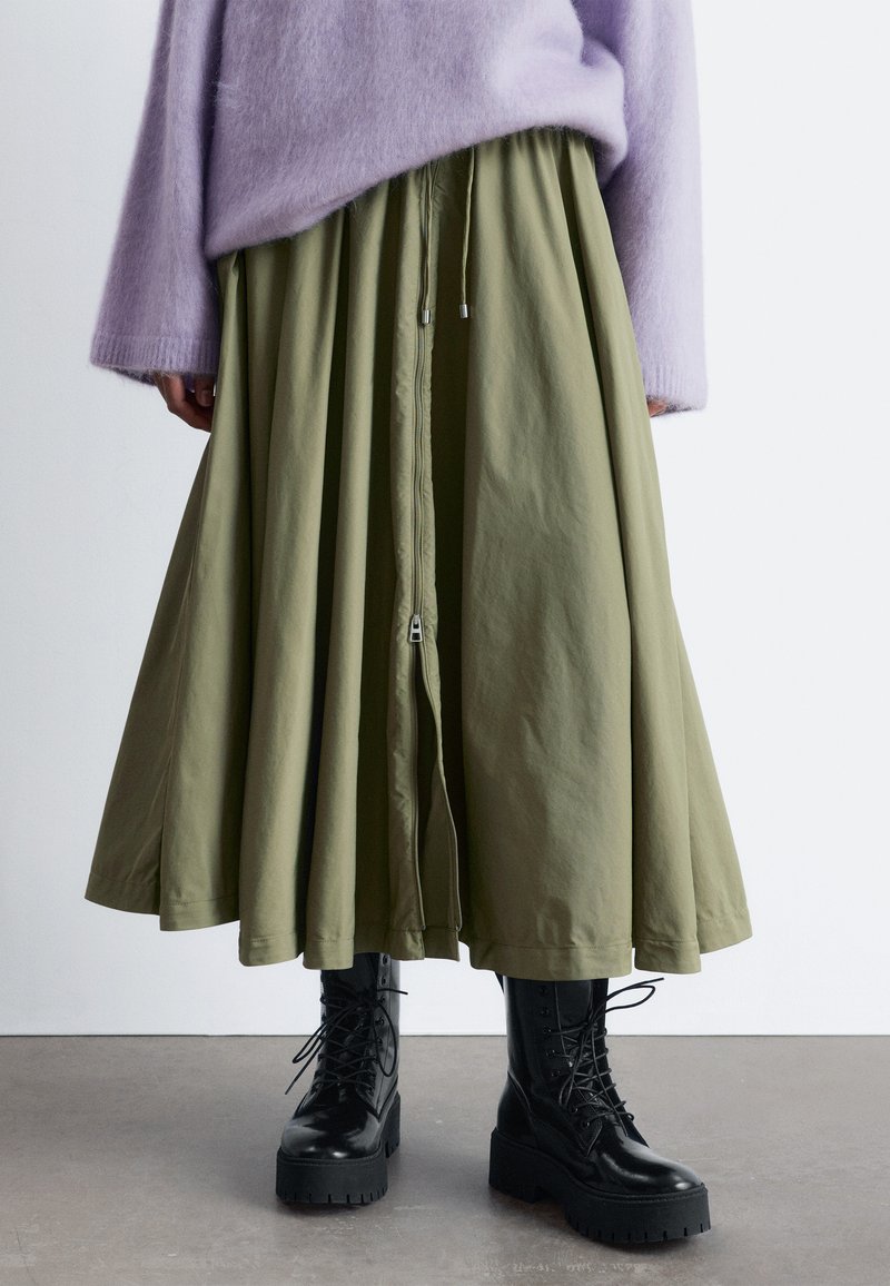 Olive green long skirt with a drawstring waist and zipper front, paired with black lace-up platform boots and a soft lavender sweater.