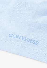Svetle modrá bavlněná látka s texturovaným povrchem, na okraji s jemným potiskem slova "CONVERSE".