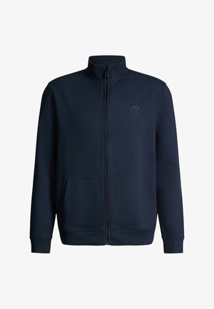 Veste zippée bleu foncé avec col montant, manches longues, poches avant et logo circulaire discret sur la poitrine gauche.