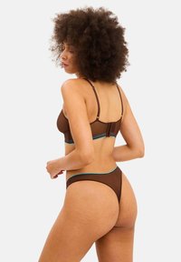 Braunes Dessous-Set mit verstellbaren Trägern, das über ein kontrastierendes türkisfarbenes Band verfügt. Das Material wirkt glatt und leicht transparent.