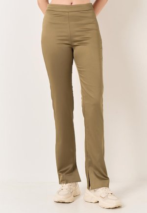 Pantalons slim en vert olive avec taille haute. Fabriqués en tissu lisse, dotés d'incisions sur l'ourlet. Associés à des baskets de couleur claire.