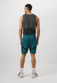 Débardeur de sport gris foncé avec un panneau noir et un short léopard turquoise avec des accents noirs, accompagné de chaussettes blanches et de chaussures grises.