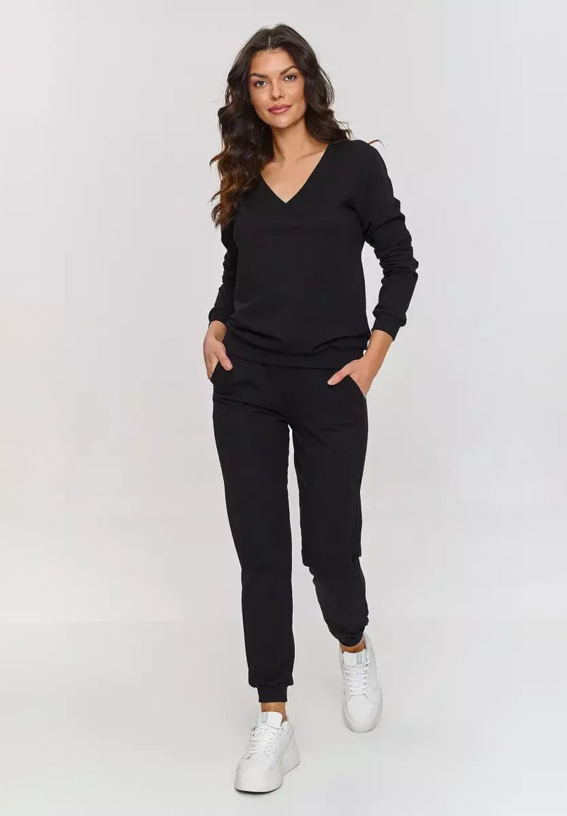 Czarny zestaw odzieży domowej składający się z bluzy z dekoltem w serek oraz zwężających się spodni, oba z prążkowanymi mankietami; zestawiony z białymi sneakersami. Gładka tekstura materiału.