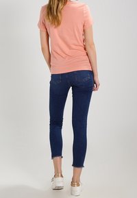 Pink short-sleeve top paired with dark blue skinny jeans featuring frayed hems, worn with white sneakers with metallic accents.