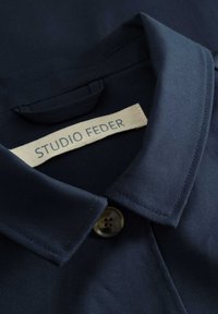 Marineblaue Hemd mit Kragen, aus glattem Stoff, ausgestattet mit einem Knopf und einem Etikett, auf dem "STUDIO FEDER" steht.